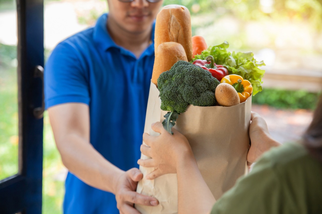Man in blue shirt handing a paper bag filled with groceries to a customer