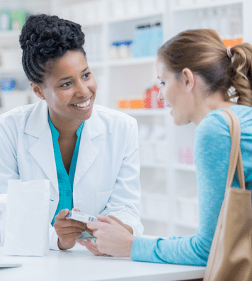 pharmacist smiling at a woman with medicine in hand