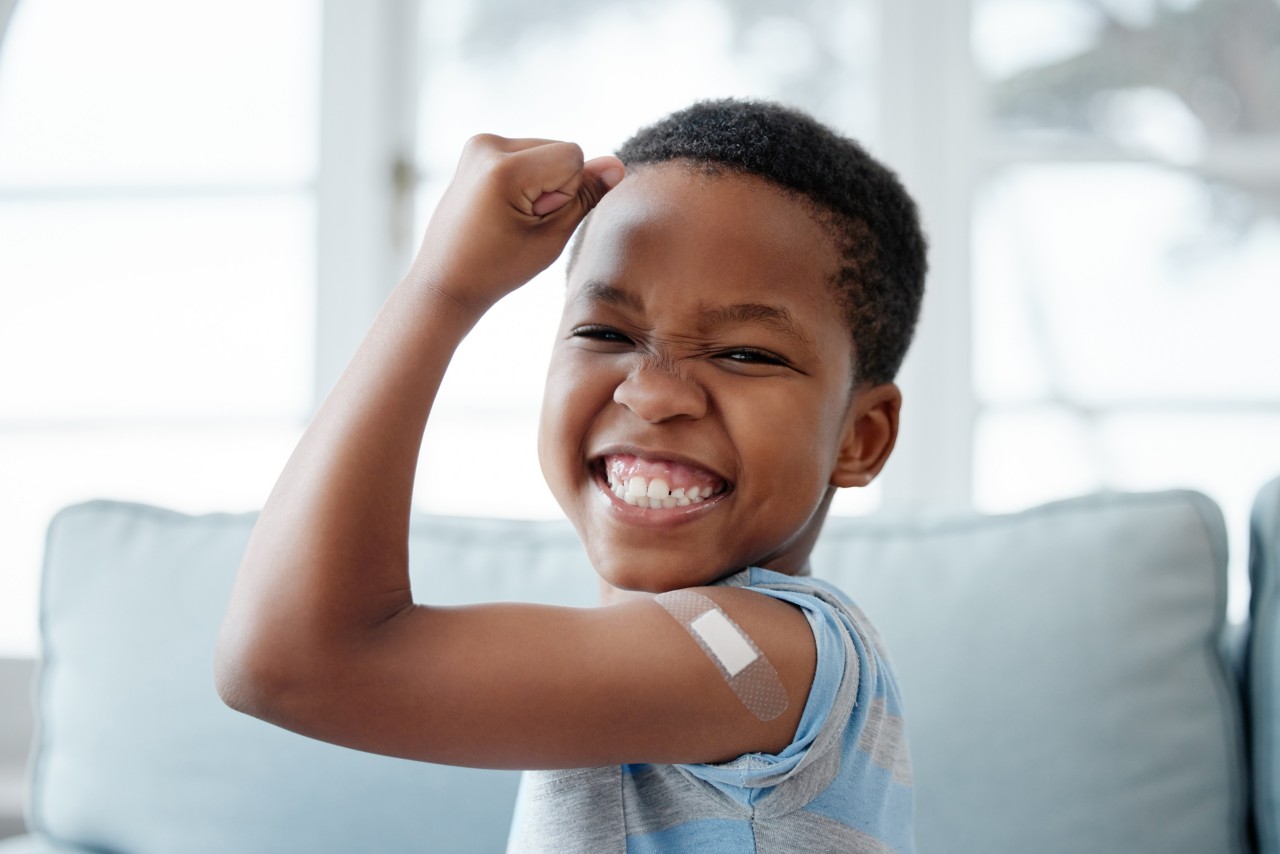 A boy smiling flexing his arm, with an adhesive bandage on his arm