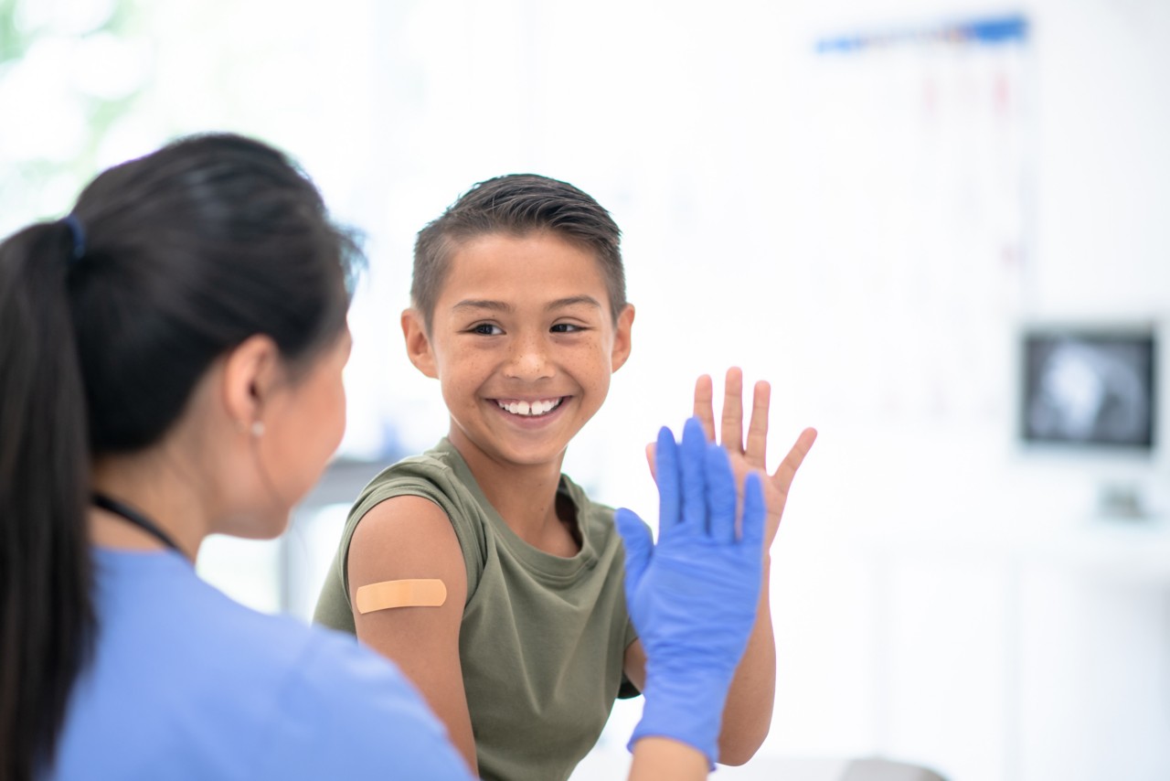 A boy with an adhesive bandage on his arm high five-ing a medical worker